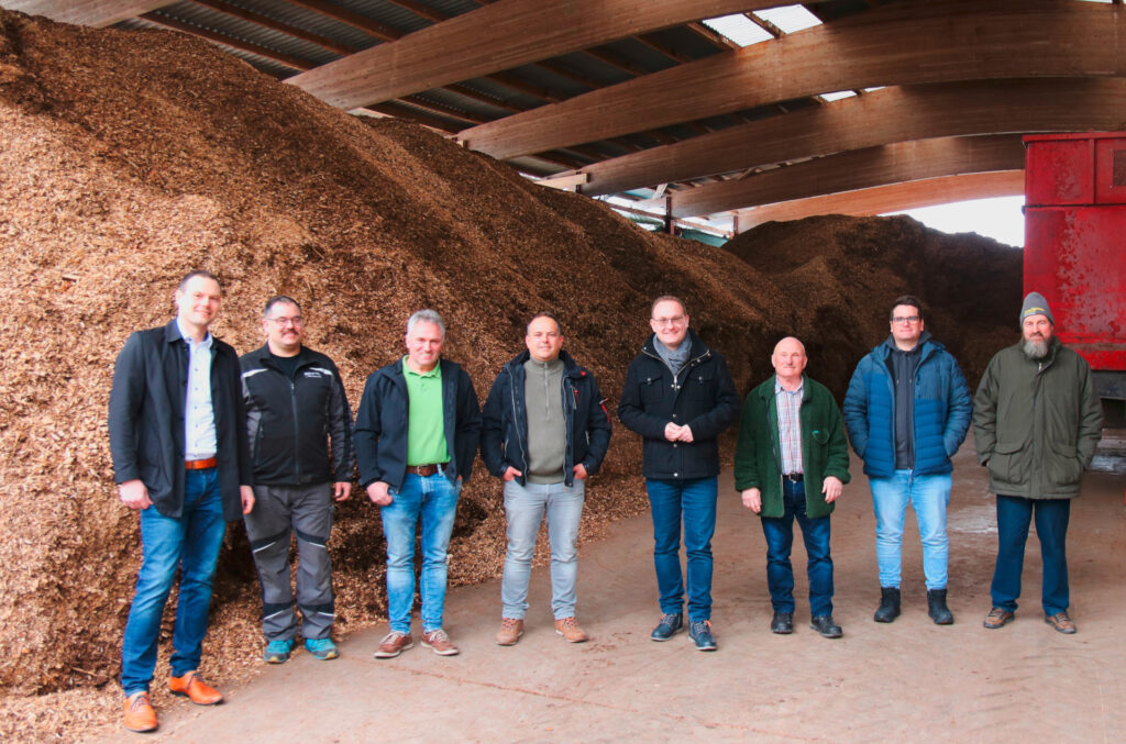 Vertreter der Stadtwerke Schwäbisch Hall und der Forstbetriebsgemeinschaft Mainhardter Wald, dessen Vorsitzender Christoph Zimmer (ganz rechts) sowie Mainhardts Bürgermeister Damian Komor (4. von rechts) und der Geschäftsführer der EMW Christian Leidig (ganz links) in der Hackschnitzellagerhalle.
